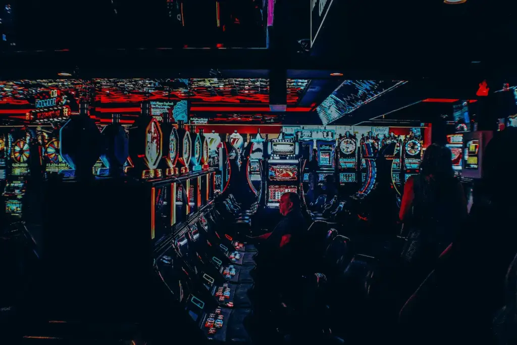Photo of a dimly lit casino with rows of slot machines and a person sitting at one