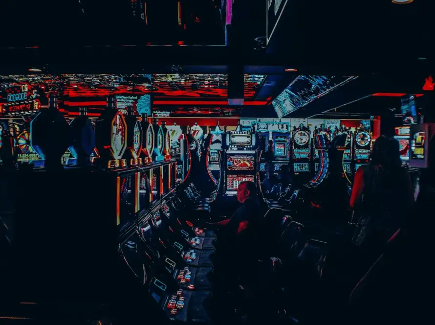 Photo of a dimly lit casino with rows of slot machines and a person sitting at one